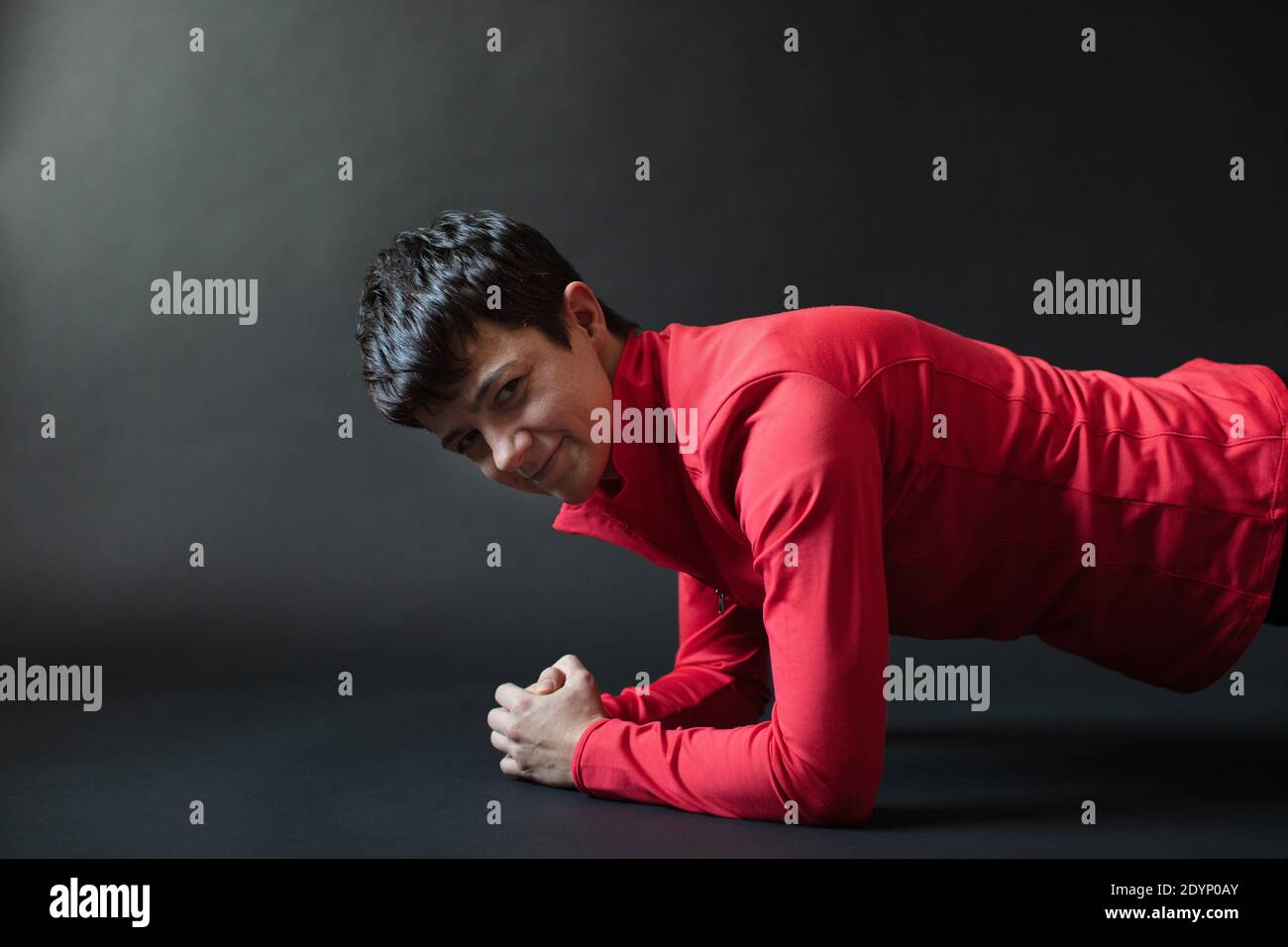 Allenatore personale femminile di 30-39 anni in abito sportivo rosso su fondo nero, che dimostra una corretta posizione della tavola. Foto Stock