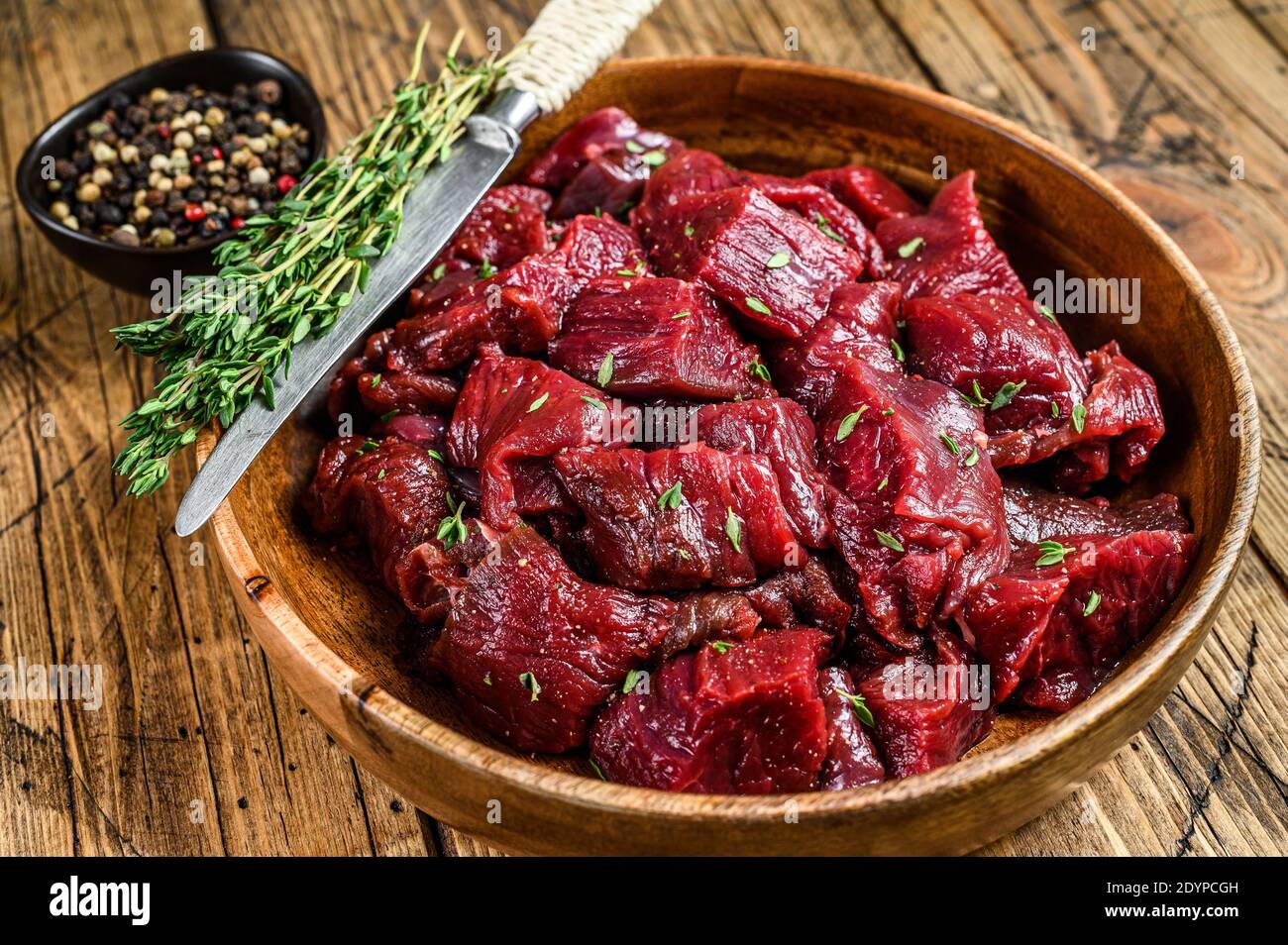 Carne di cervo selvatico tagliata grezza per un goulash in un piatto di legno. Sfondo di legno. Vista dall'alto Foto Stock
