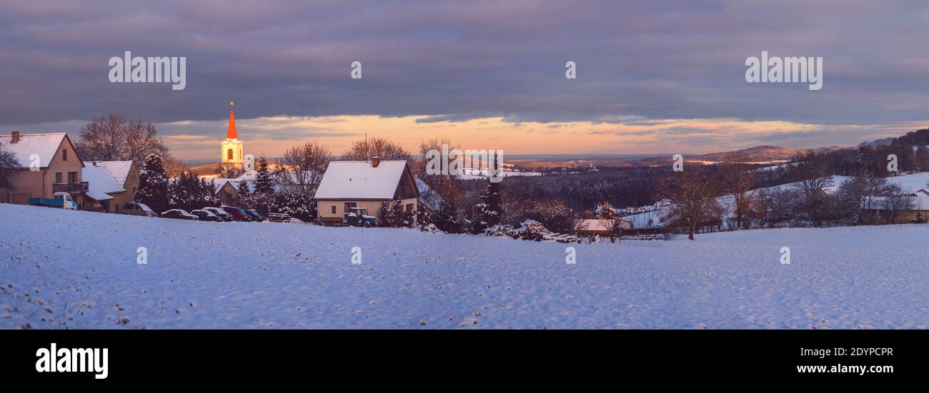 Paesaggio invernale con campo nevoso e villaggio, luce serale che illumina la chiesa, Vezovata piano, repubblica Ceca Foto Stock