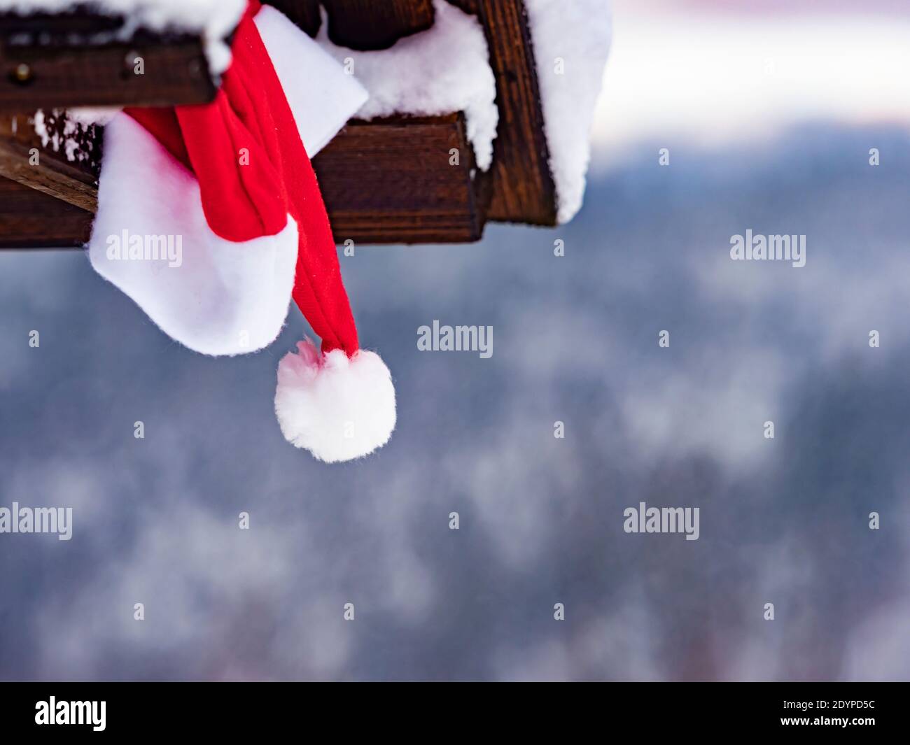 Cappellino rosso Babbo Natale sotto tetto cabina in legno inverno mostra il panorama paesaggistico paesaggio panoramico isolato da sfondo sfocato Foto Stock