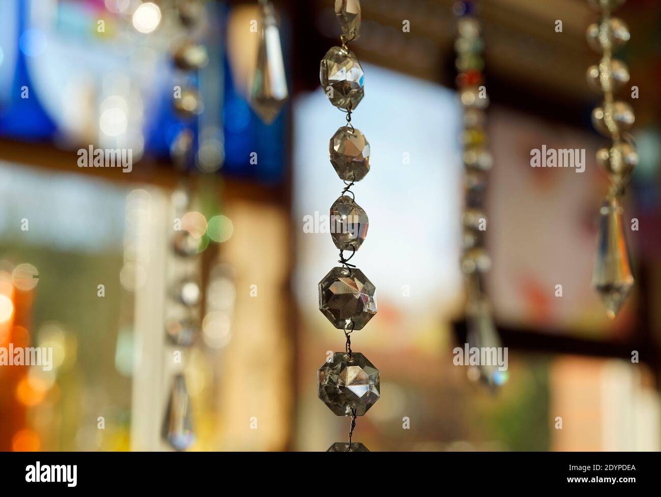 Cordoncino con cristalli di lampadario che catturano la luce. Sullo sfondo altri cordoni di cristallo, fiasche di vetro e altri oggetti. Feng Shui Foto Stock