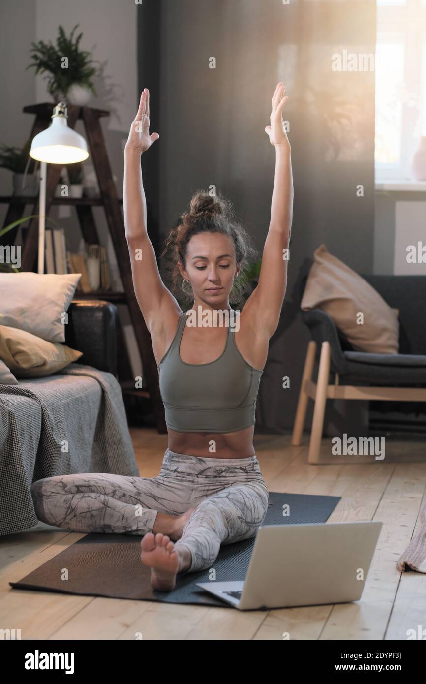 Giovane donna seduta sul pavimento di fronte al computer portatile e meditating online in camera Foto Stock
