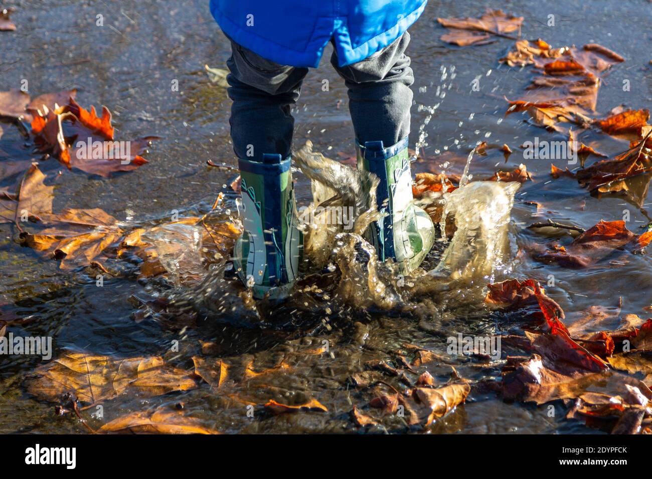 le gambe di un bambino che indossa i wellies saltando in pudddles schizzi Foto Stock