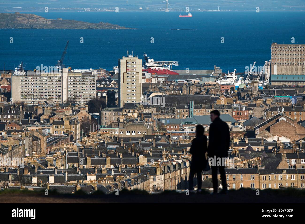La silhouette di una coppia che si trova sulla collina di Calton guardando verso nord verso Leith e il Firth of Forth a Edimburgo, Scozia, Regno Unito. Foto Stock