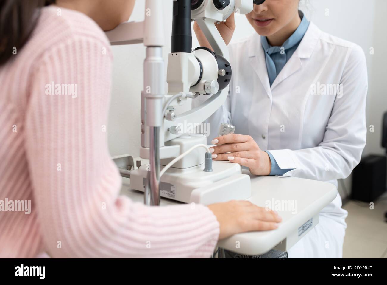Giovane oftalmologo femminile in whitecoat utilizzando apparecchiature mediche per il controllo vista di una studentessa elementare nelle cliniche contemporanee Foto Stock