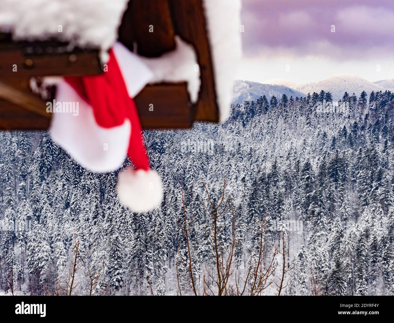 Cappellino rosso Babbo Natale fissato sotto il tetto della cabina in legno Spettacolo invernale paesaggio panoramico panorama Foto Stock