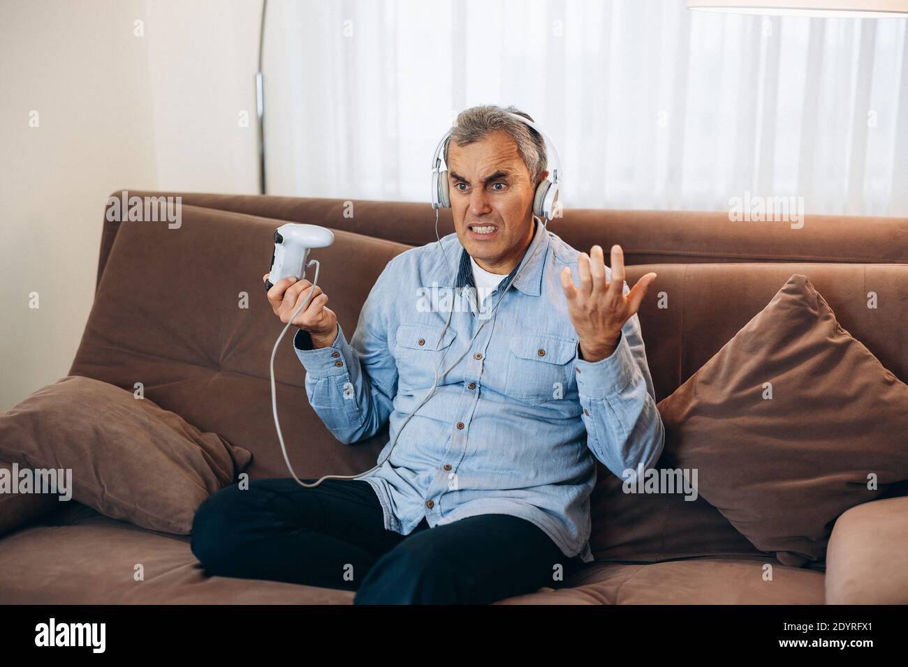 Gioco finito. Uomo medio anziano che gioca usando il joystick di controllo della console. Intrattenimento durante il blocco. Gioco perso. Soggiorno sullo sfondo Foto Stock