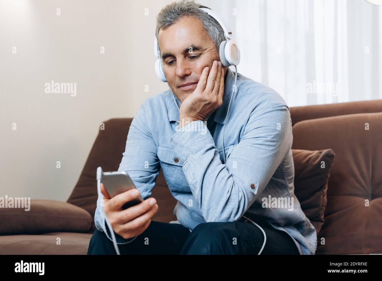 L'uomo anziano con le cuffie sta guardando un film interessante dal suo telefono. Intrattenimento durante il blocco. L'uomo maturo si rilassa guardando il video Foto Stock