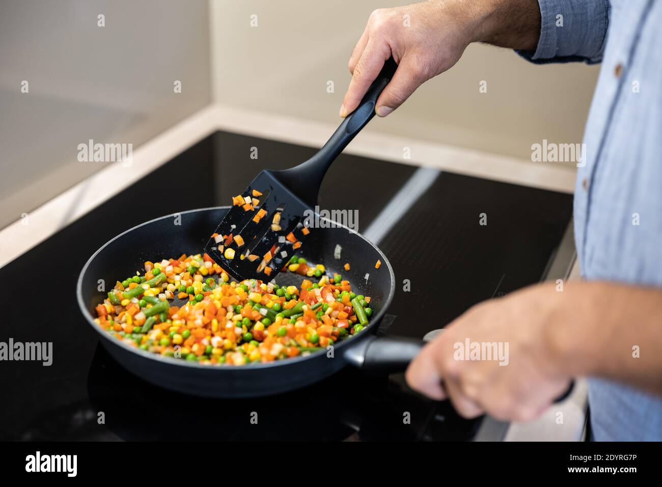 Stufate le verdure colorate in una padella. Spatola e piatto di miscelazione per uomo adulto. Concetto di cibo sano. Elettrodomestici da cucina moderni. Sano e gustoso Foto Stock