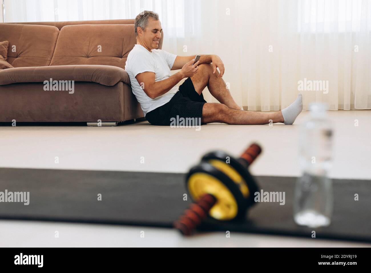 Uomo pigro anziano che sta testando sullo smartphone o cerca alcuni memo. Procrastinazione durante il fitness. Metti giù il telefono se vuoi un forte e sano Foto Stock