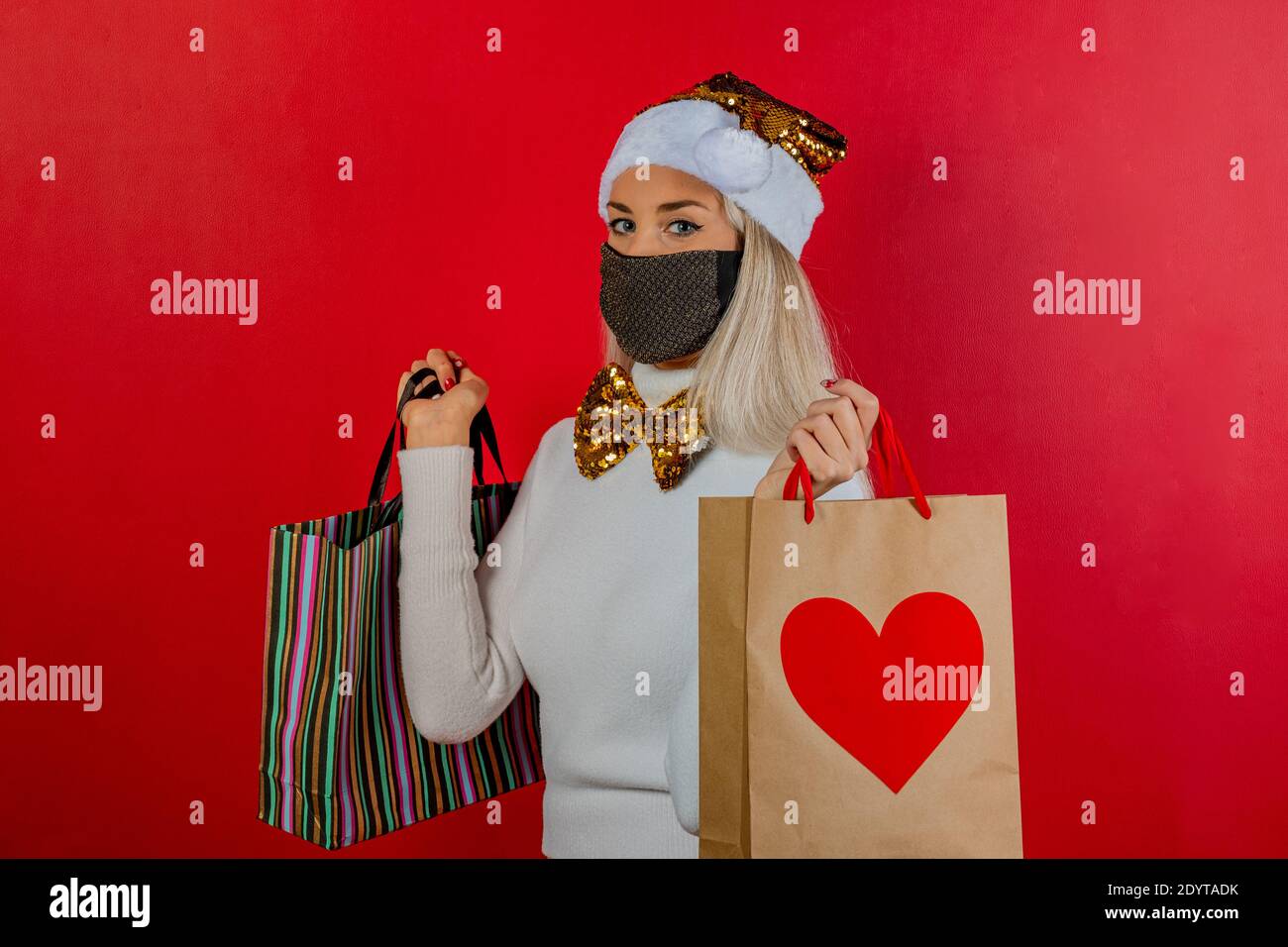 Moda ragazza shopping in abito bianco con maschera oro protettivo, oro papillon e cappellino di Natale per la prevenzione da coronavirus Covid19 pandemia. Foto Stock