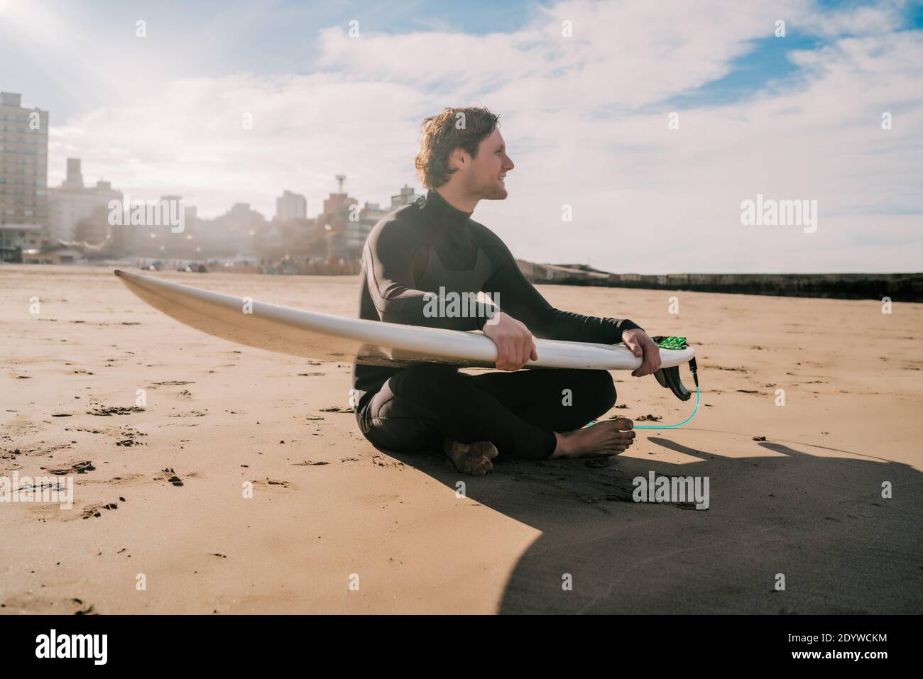 Surfista seduto sulla spiaggia di sabbia con tavola da surf. Foto Stock