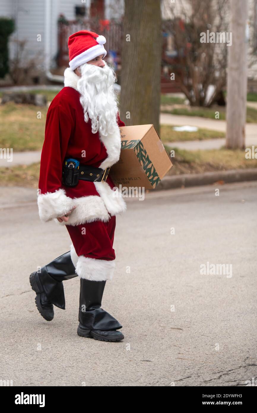 Winneconne, WI-23 dicembre 2020: Un vettore di lettera del lavoratore postale USPS è vestito in su come Babbo Natale mentre consegna un pacchetto ad una casa. Foto Stock