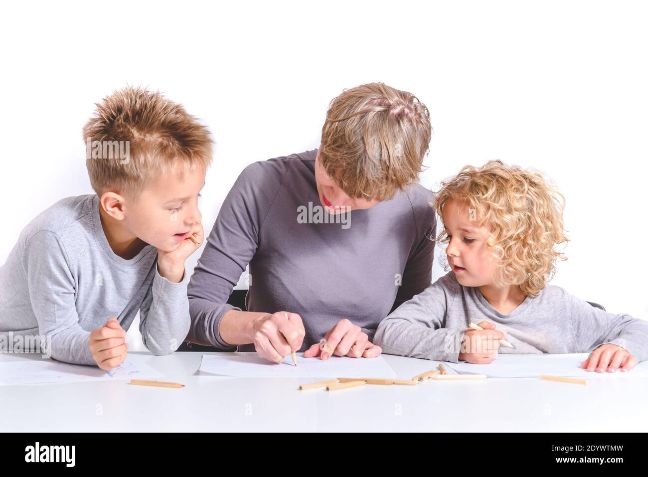 bionda caucasica bella giovane madre che scrive con la matita su una carta con i bambini su entrambi i lati guardando. Concetto di scuola domestica Foto Stock