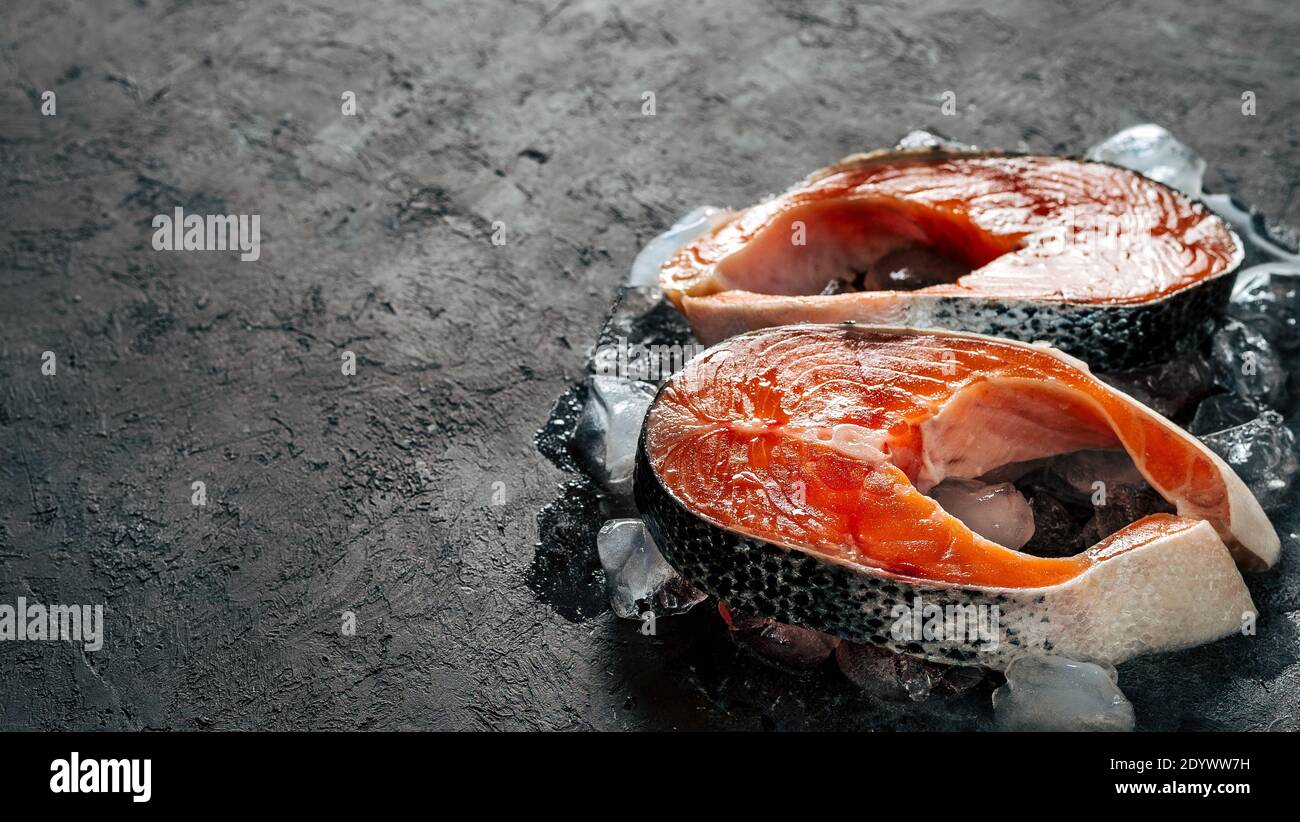 Due bistecche di salmone selvatico crudo su ghiaccio su sfondo nero testurizzato. Bistecche di salmone con spazio per la copia a sinistra. Banner orizzontale Foto Stock