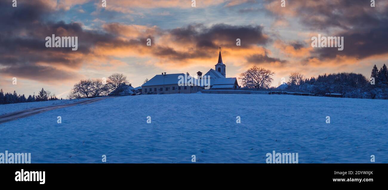 Villaggio con una chiesa su una collina al tramonto in inverno, bel cielo con nuvole illuminate, Vezovata piano, repubblica Ceca Foto Stock