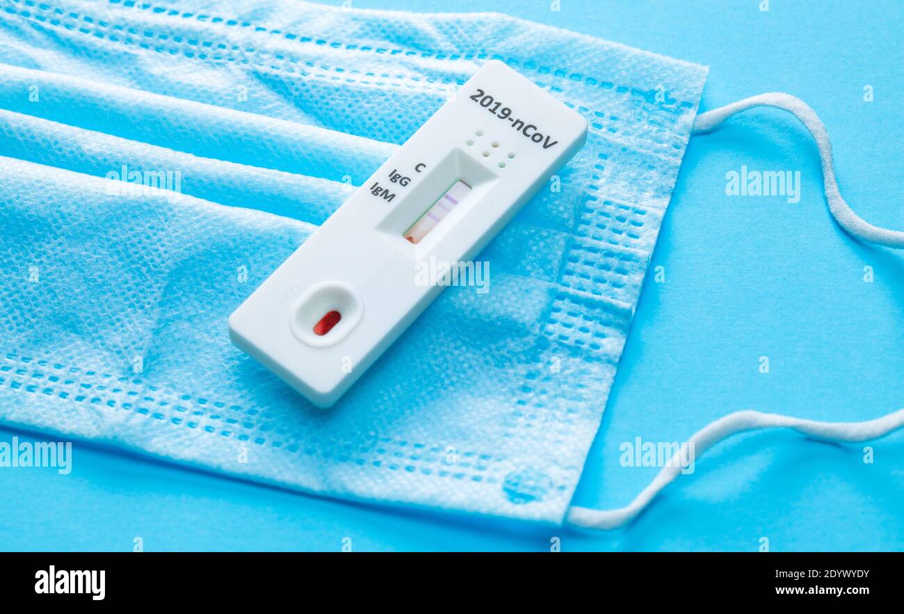 Esame del sangue domestico per COVID-19 su sfondo blu con una maschera medica. Foto Stock