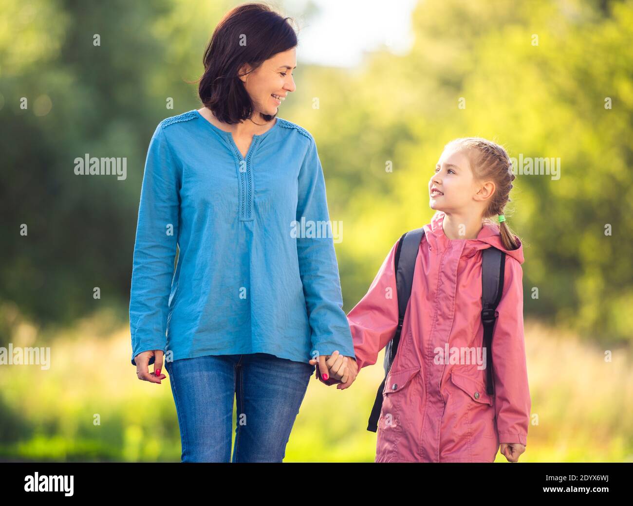 Madre che conduce la figlia a scuola su sfondo soleggiato natura Foto Stock