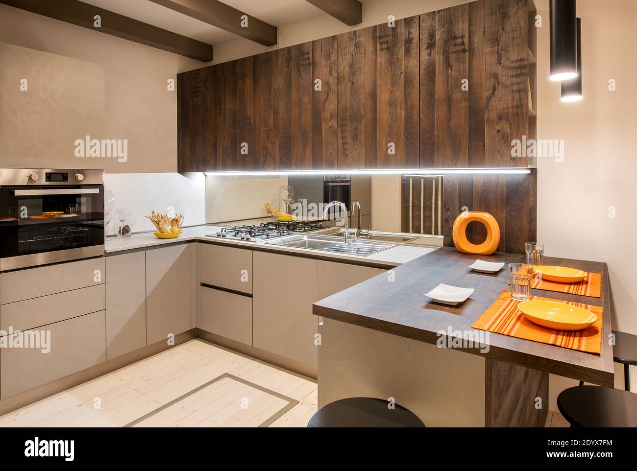Interni di cucina moderna con accenti arancioni e neutri armadi di colore beige con illuminazione incassata Foto Stock