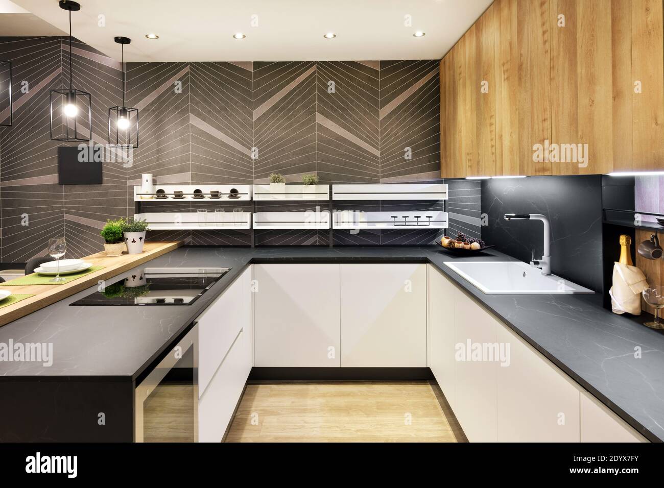Interno cucina lungo e stretto con elettrodomestici integrati e bianco armadietti anteriori illuminati da plafoniere in vista retroscile Foto Stock
