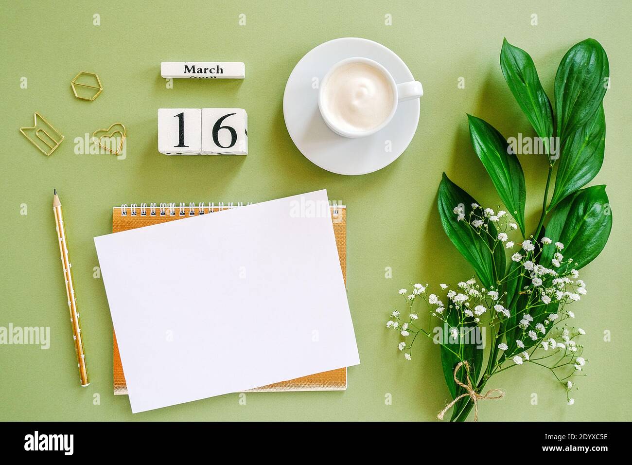 Cubi di legno calendario marzo 16. Blocco note, tazza di caffè, fiori di bouquet su sfondo verde. Concept ciao spring Creative Top view Flat Lay Mock up. Foto Stock