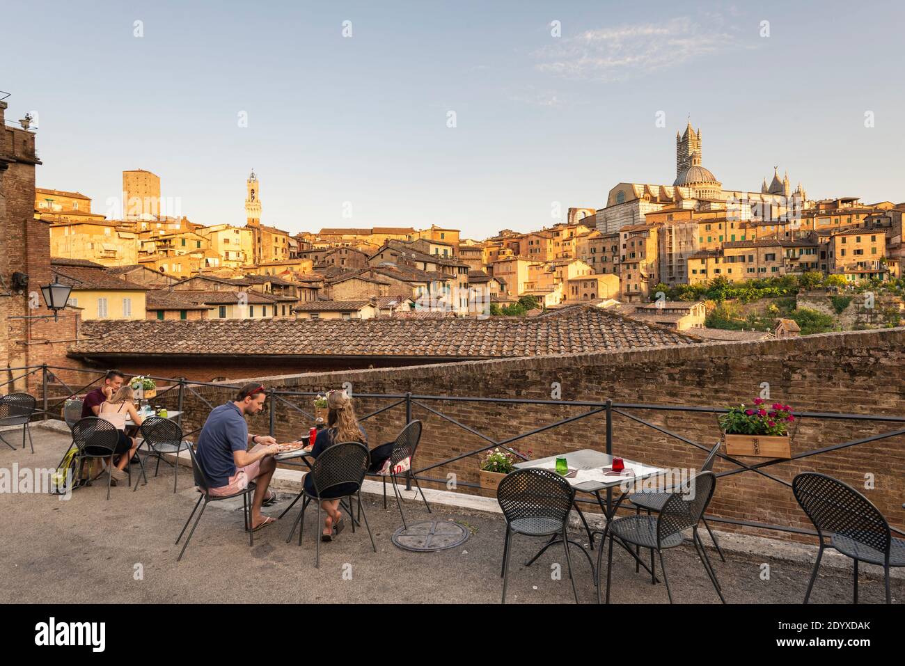 Le coppie giovani cenano sulla terrazza di un ristorante che si affaccia sul centro storico medievale di Siena al sole della sera, Toscana, Italia Foto Stock