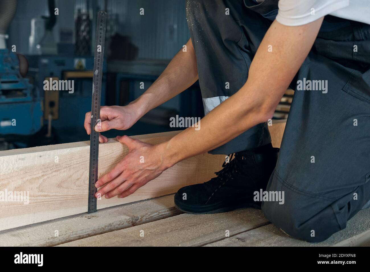 Un giovane lavora in un negozio di carpenteria. Un dipendente misura il legno con un righello Foto Stock