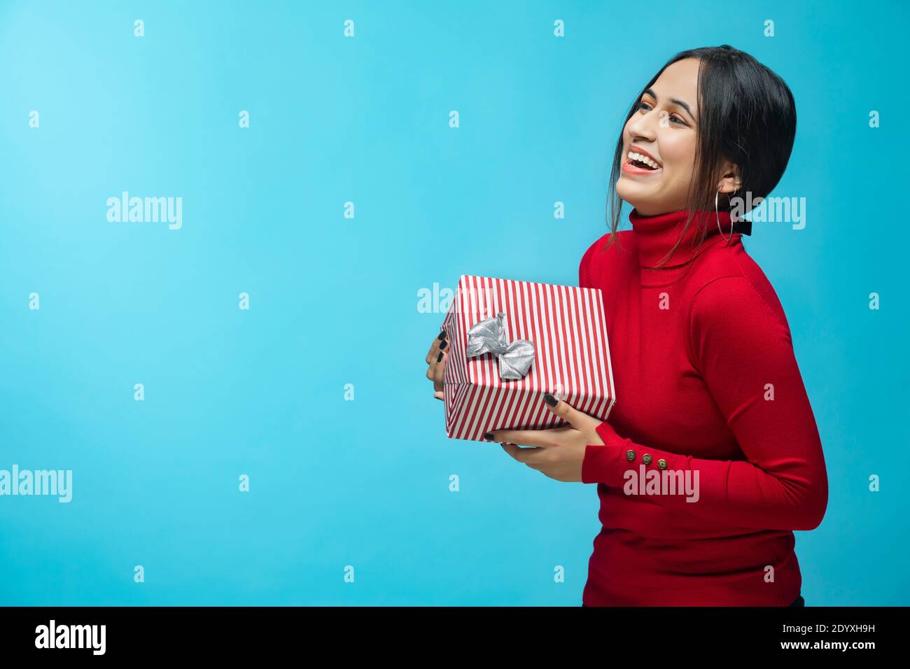Ritratto di giovane donna che indossa una felpa rossa e porta un regalo scatola in mano Foto Stock