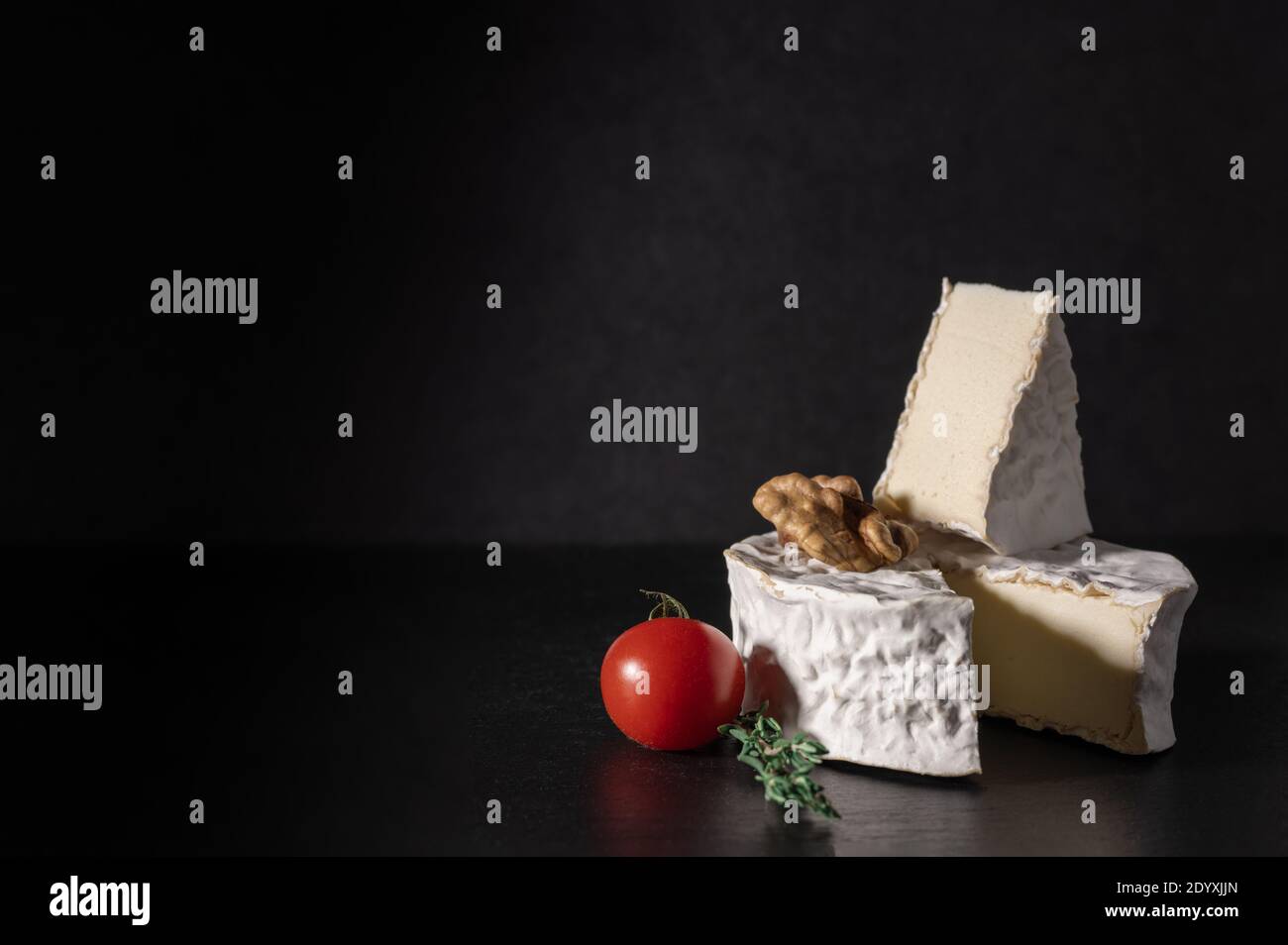 brie con pomodoro e noce su fondo nero. Tipo Brie di formaggio. Camembert. Formaggio Brie fresco e una fetta su tavola di pietra. Italiano, Francese Foto Stock