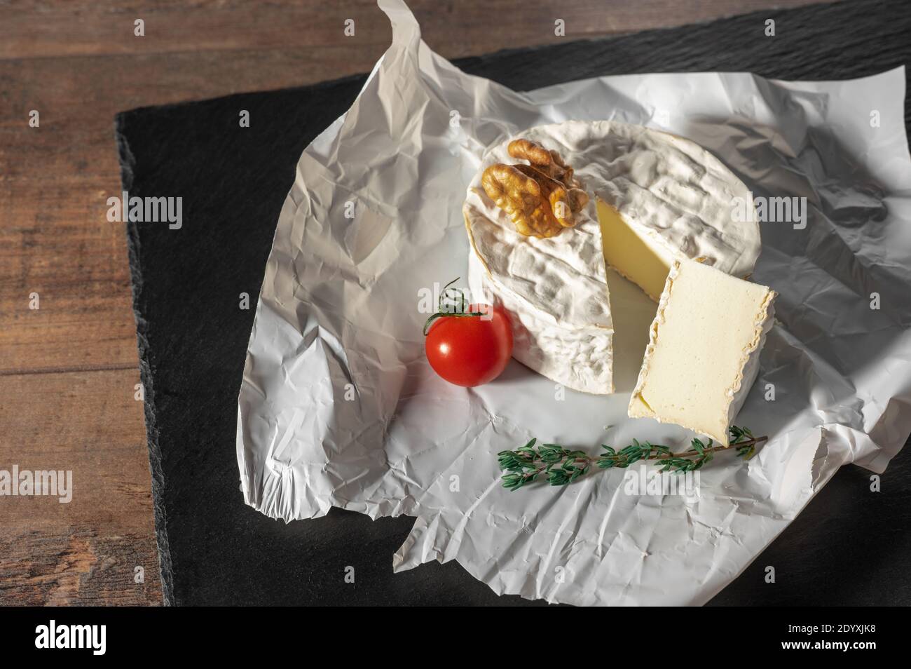 Delizioso formaggio brie, noci e pomodoro su carta su sfondo nero ardesia. Tipo Brie di formaggio. Camembert. Formaggio Brie fresco e una fetta di pietra b Foto Stock