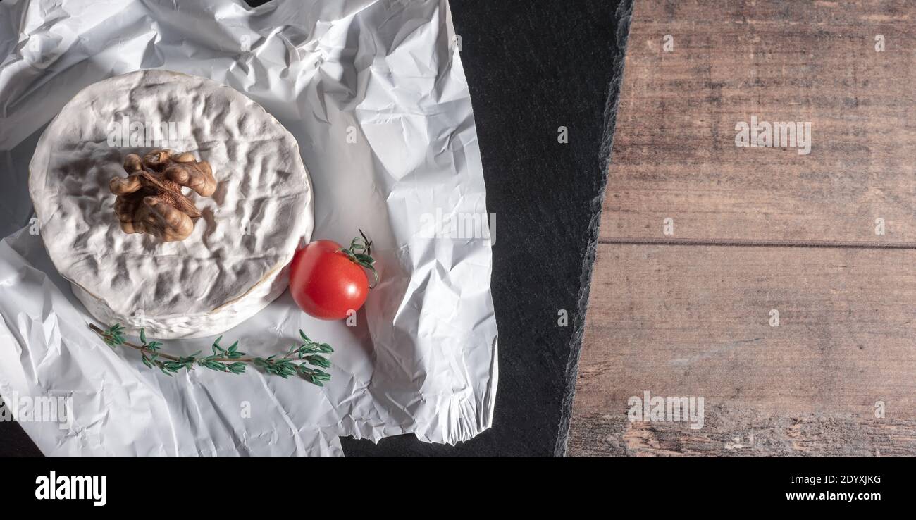 Formaggio con noci e pomodoro. Delizioso formaggio brie su sfondo nero. Tipo Brie di formaggio. Camembert. Formaggio Brie fresco e una fetta su tavola di pietra. Foto Stock