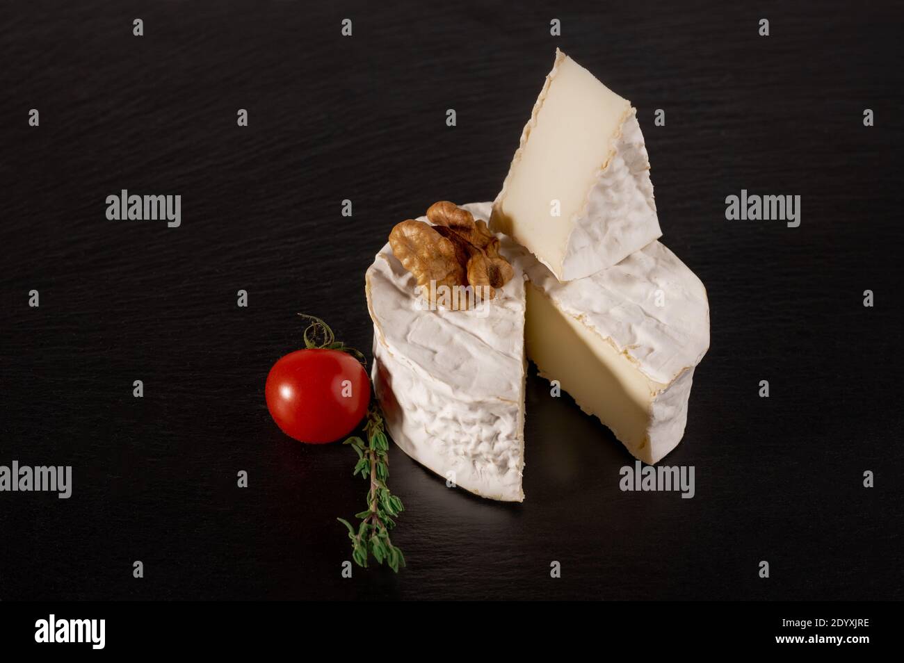 brie con pomodoro e noce su fondo nero. Tipo Brie di formaggio. Camembert. Formaggio Brie fresco e una fetta su tavola di pietra. Italiano, Francese Foto Stock