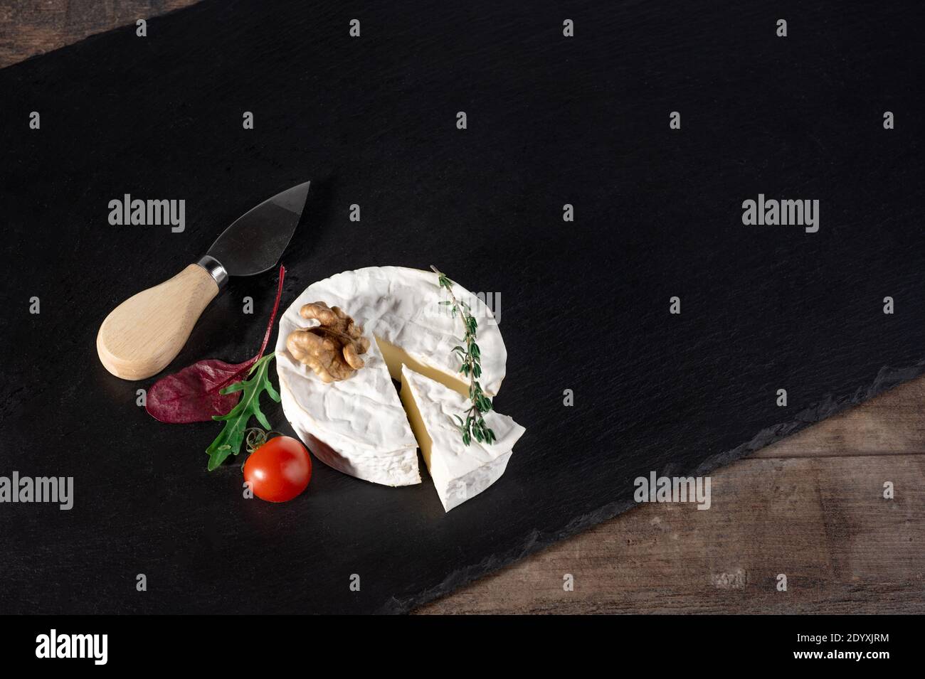 Delizioso formaggio brie con pomodoro e noce su sfondo nero e rustico tavolo in legno. Tipo Brie di formaggio. Camembert. Brie fresco e un slic Foto Stock