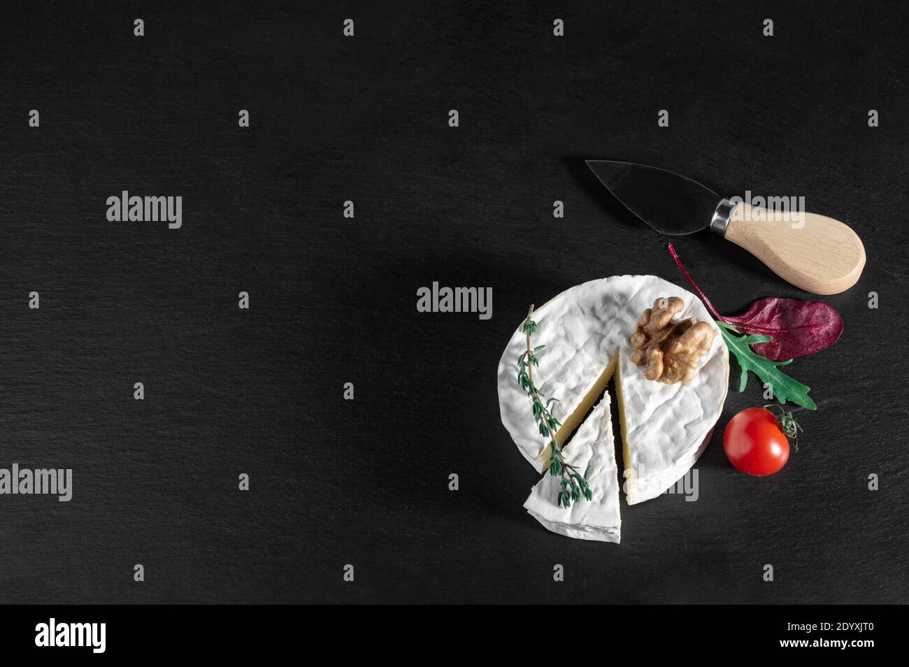 Delizioso formaggio brie con pomodoro e noce su sfondo nero. Tipo Brie di formaggio. Camembert. Formaggio Brie fresco e una fetta su tavola di pietra. Italia Foto Stock