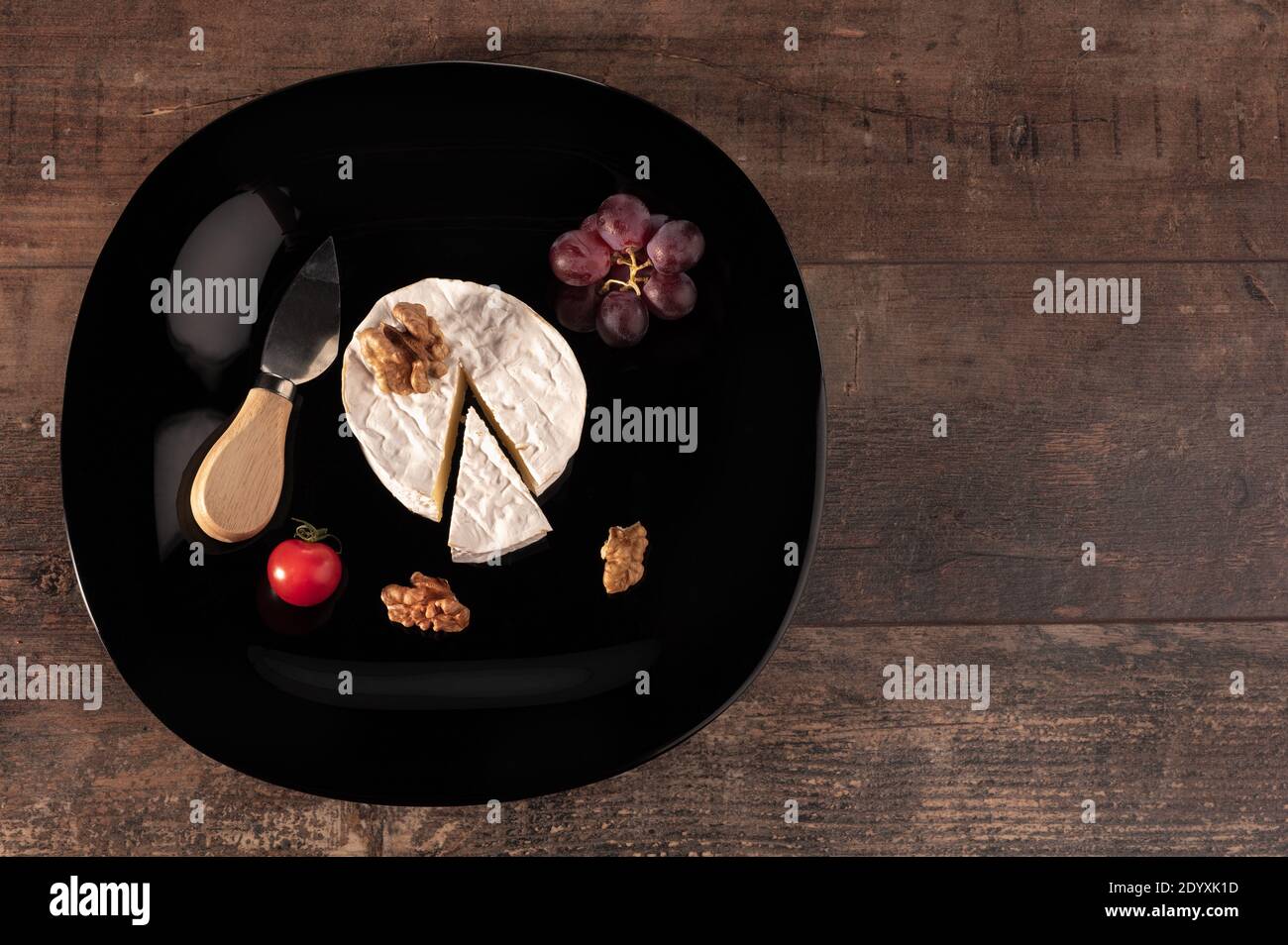 Delizioso formaggio brie su piatto nero. Tavola rustica in legno. Tipo Brie di formaggio. Camembert. Brie fresco e una fetta con coltello. Italiano, Francese c Foto Stock