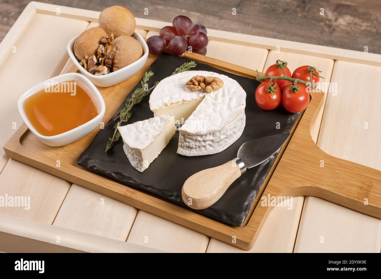 vassoio di legno per la colazione con formaggio brie, miele, noci, pomodoro. colazione al formaggio sul vassoio di legno con piatto nero Foto Stock