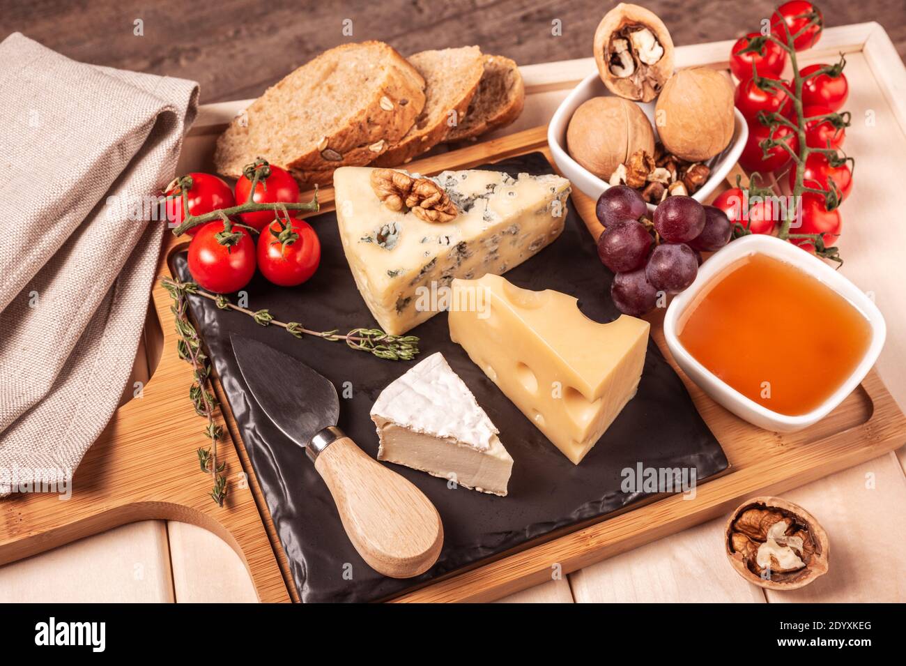 vassoio in legno per la colazione con assortimento di formaggi, miele, noci, pomodoro. dessert al formaggio sul vassoio in legno con piatto nero. immagine tonata Foto Stock