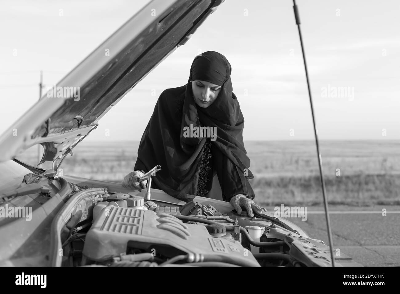 Donna islamica conducente riparando auto su strada vuota. Bianco e nero Foto Stock