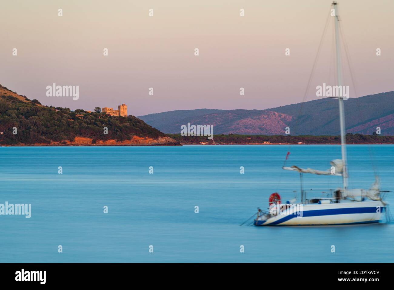 La torre fortificata Torre di Talamonaccio sulla baia di Talamone si illumina al crepuscolo serale al tramonto, Toscana, Italia Foto Stock