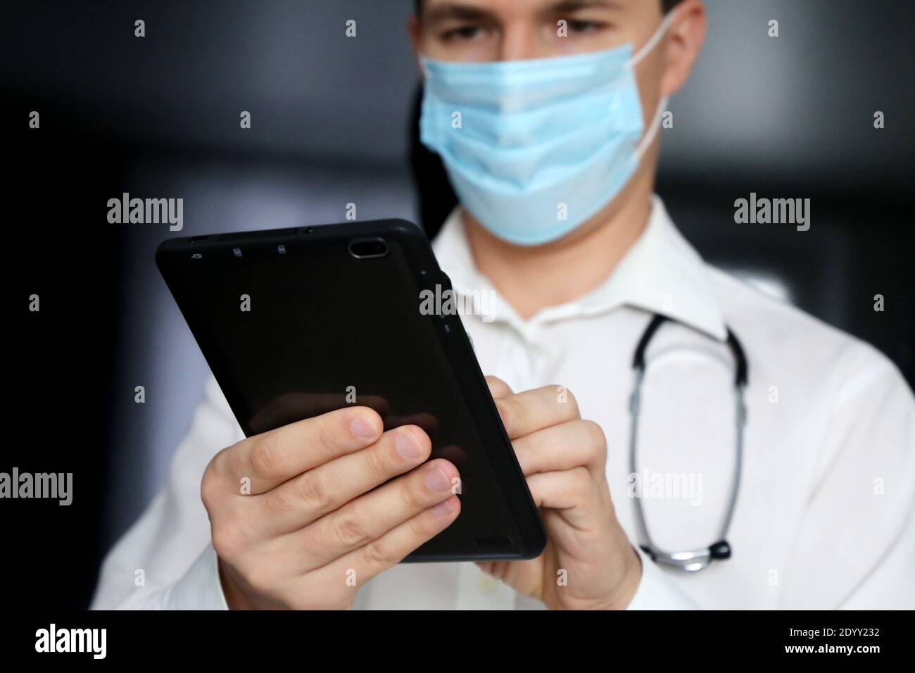 Medico uomo in una maschera medica con un PC tablet in mani. Lavoro del personale medico durante l'epidemia di coronavirus del covid-19 Foto Stock