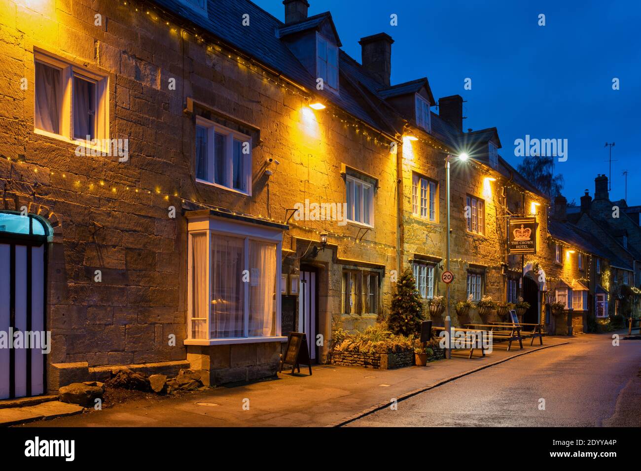 Luci di Natale di notte al di fuori delle case e il Crown hotel nella strada alta. Blockley, Cotswolds, Gloucestershire, Inghilterra Foto Stock