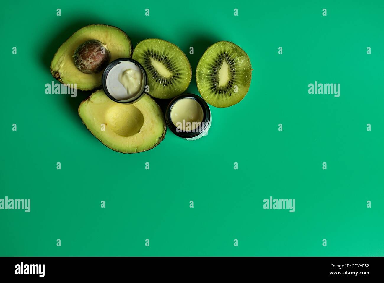 Semi di kiwi, pera di avocado e crema oculare di olio d'uva usata per trattare le aree oculari. Crema per gli occhi e kiwi e avocado a fette su sfondo verde in studio Foto Stock