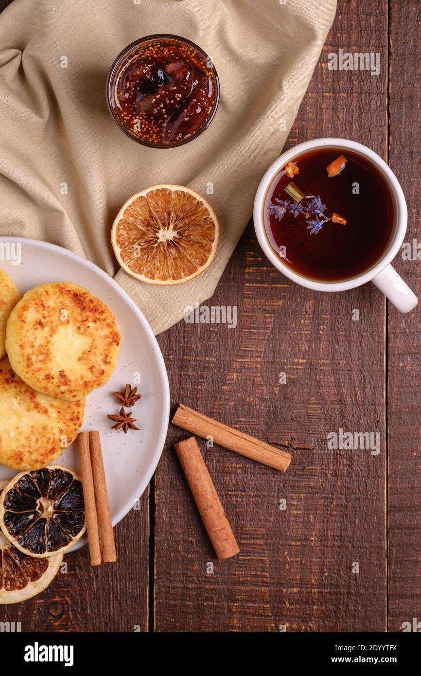 Frittelle di formaggio di cottage con tè nero aromatico caldo con confettura di fichi, umore della colazione di Natale con anice, cannella e agrumi secchi su sfondo di legno, Foto Stock