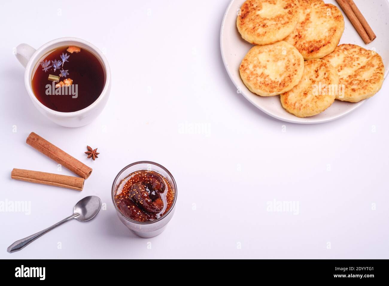 Frittelle di formaggio cottage con marmellata di fichi e tè nero aromatico caldo, umore della colazione di Natale con anice e cannella su sfondo bianco, vista angolare Foto Stock
