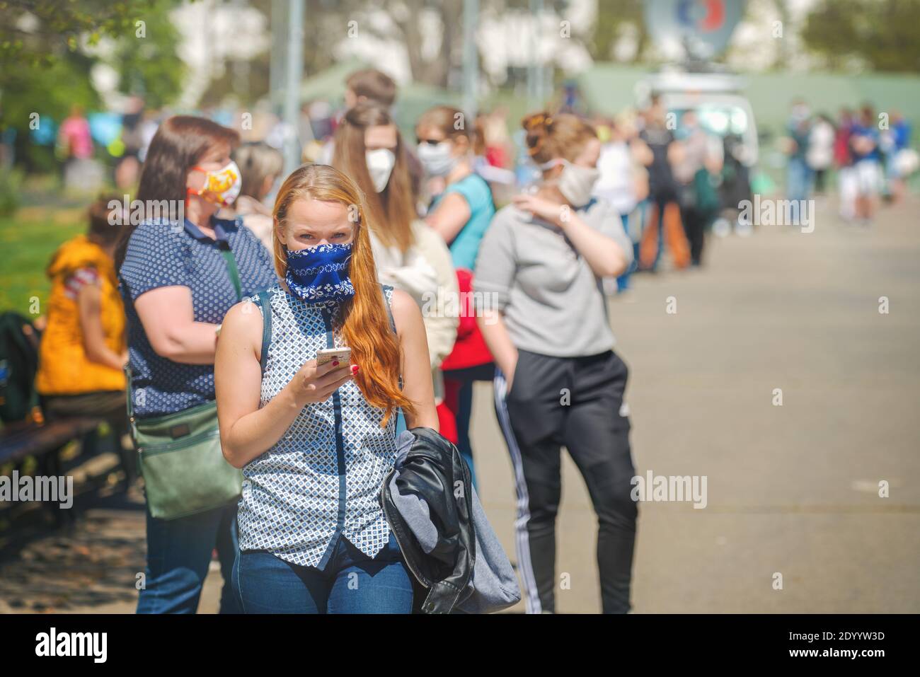 Donna con una maschera di tessuto che attende in lunga coda di persone per un test come parte di uno studio sull'immunità collettiva contro il virus corona. Foto Stock