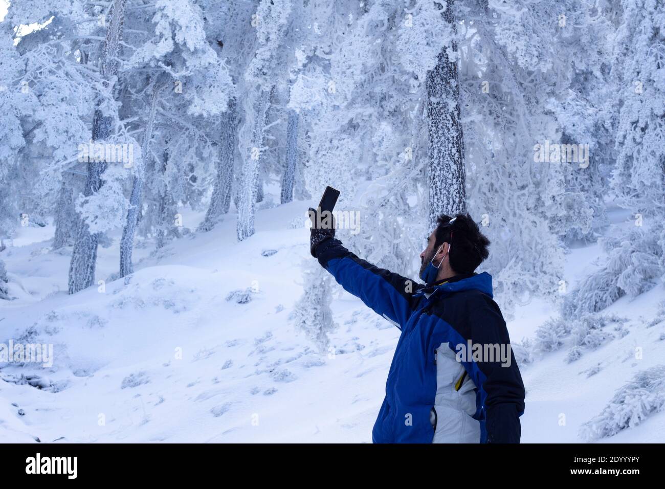 un uomo di mezza età cerca il segnale wifi su una montagna innevata. L'uomo indossa una maschera abbassata. Connessione wifi in natura profonda Foto Stock
