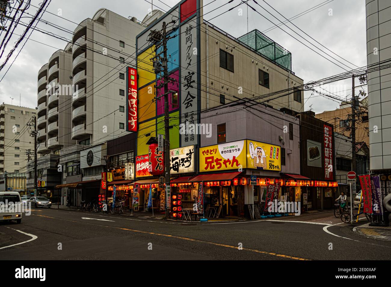 Insegne luminose colorate pubblicizzano yakitori, gyoza e frutti di mare su un angolo di strada a Shizuoka, Prefettura di Shizuoka, Giappone, di sera – tra cui il ristorante di yakitori "Anichan", la catena di izakaya "Umi-hōzuki" e il ristorante "Gyōza Kenkyūjo" (Istituto di ricerca sui gyoza). Foto Stock