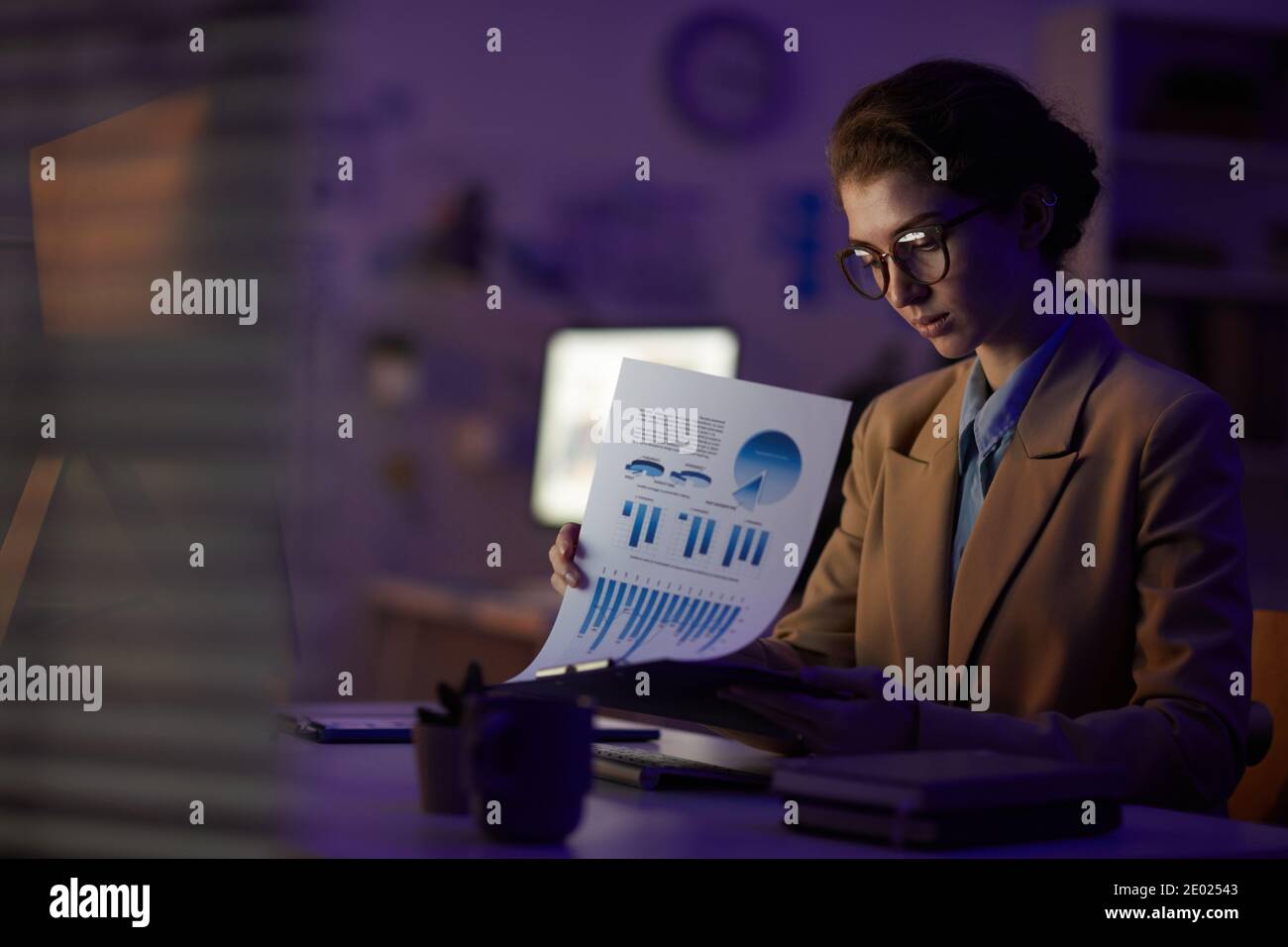 Giovane donna responsabile finanziario seduto alla scrivania guardando attraverso i documenti a tarda notte in camera d'ufficio, spazio per la copia Foto Stock