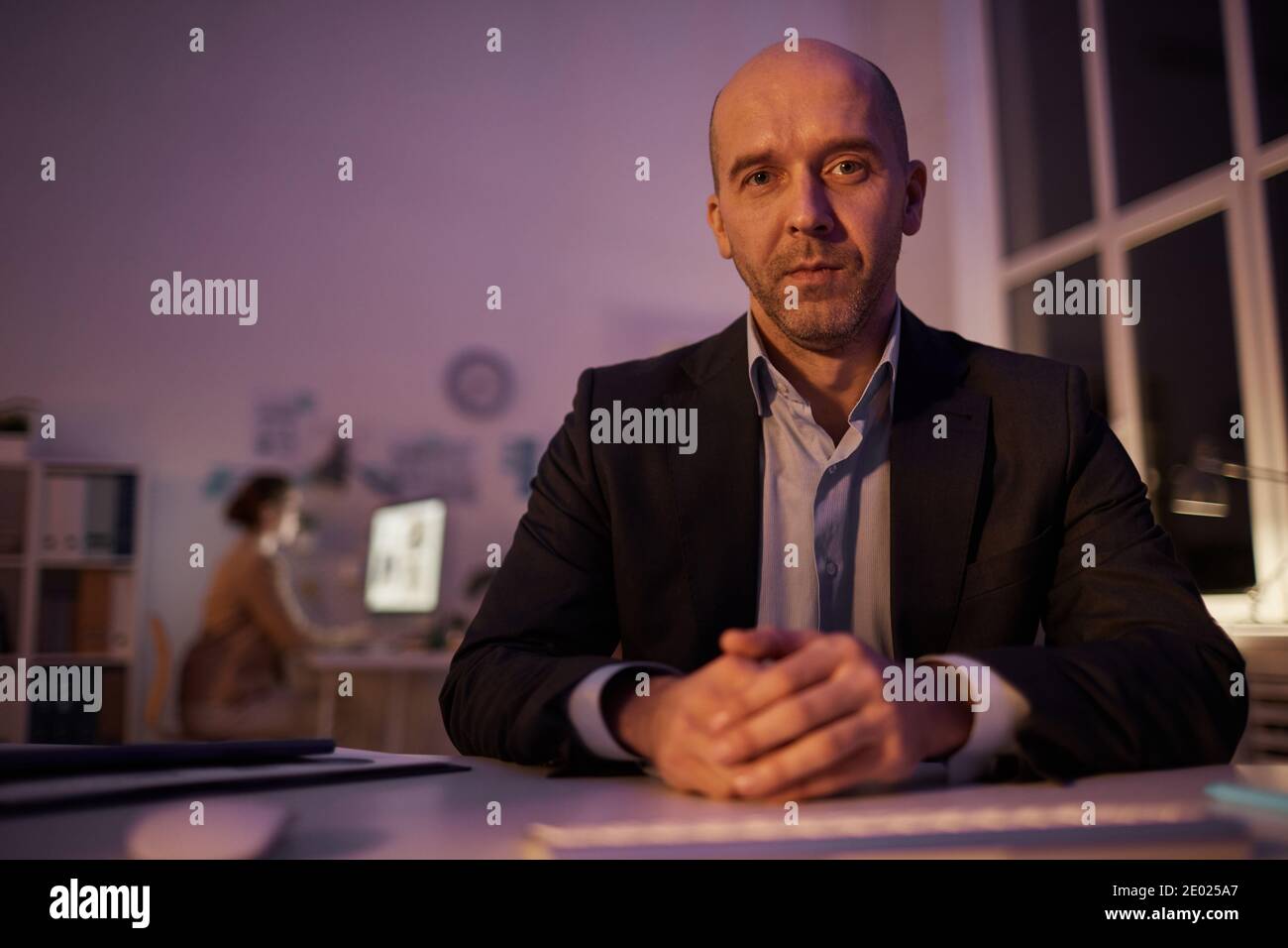 Ritratto della moderna persona d'affari caucasica seduta alla scrivania stanza dell'ufficio a tarda sera guardando la macchina fotografica Foto Stock