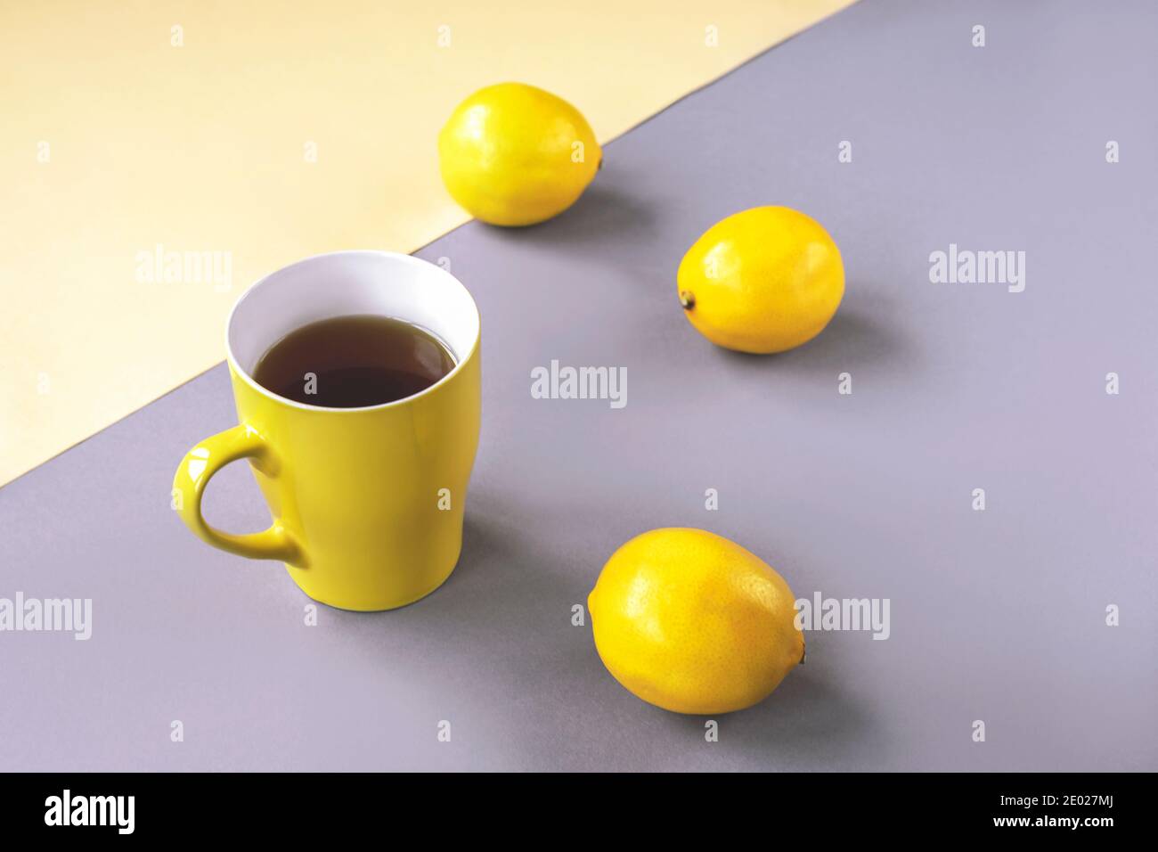 Tazza gialla di tè e limoni su sfondo grigio. Colori alla moda 2021 Foto Stock